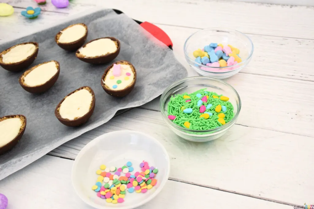 Eggs filled with cheesecake and being decorated with pastel sprinkles and other small candies.