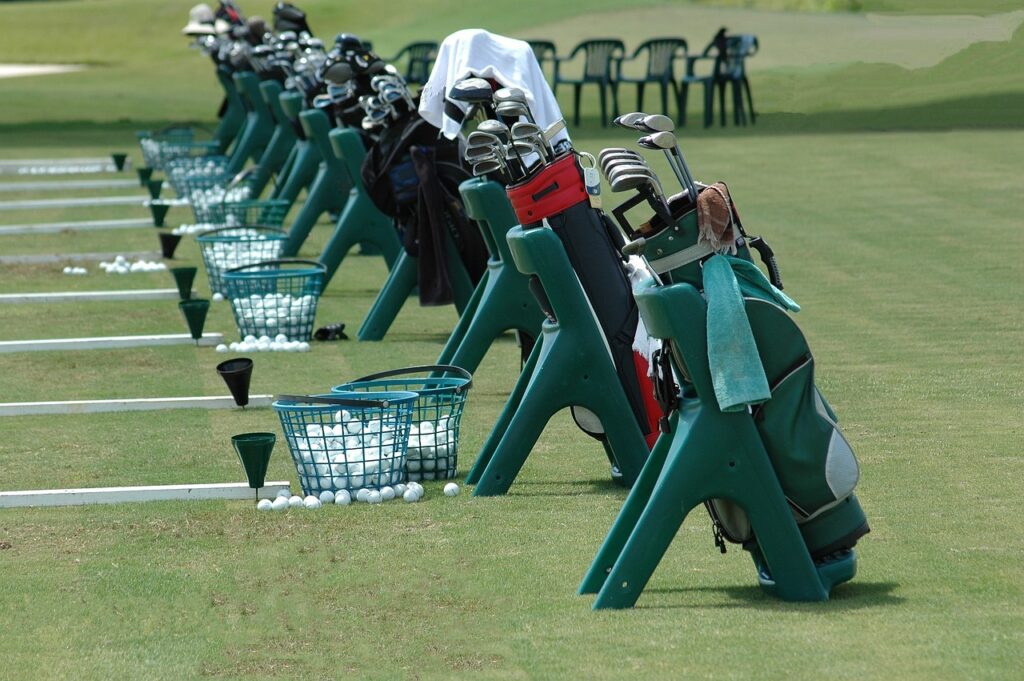 A row of golfing equipment on a putting green for newbie golfers to practice.
