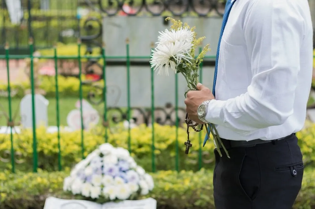 Мужчина в костюме возлагает белые цветы на могилу после похорон