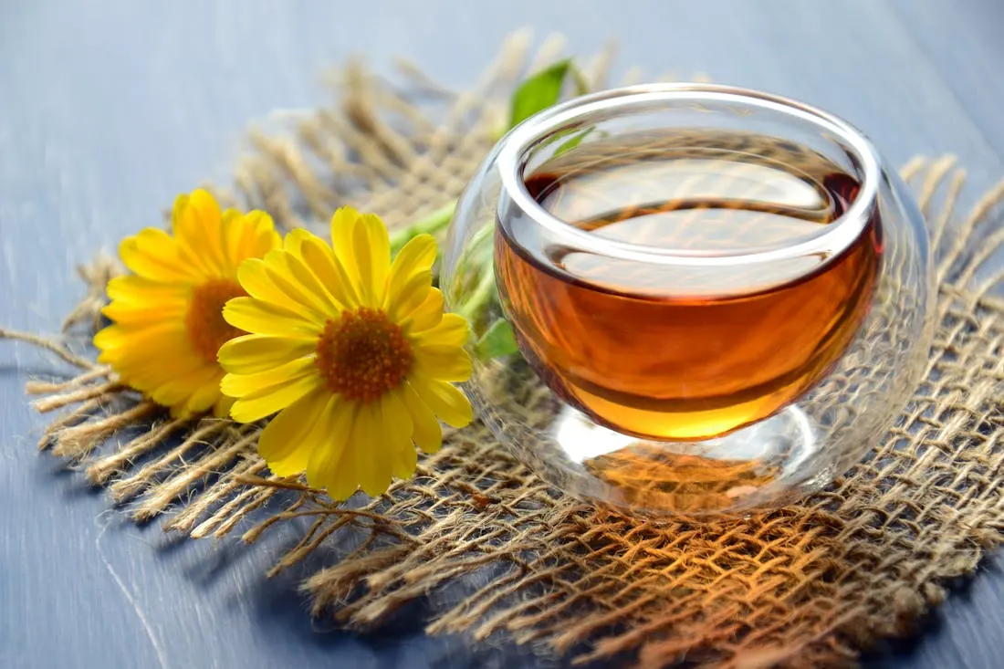 A glass of green tea sitting on a piece of burlap next to two flowers. There are many reasons to make the switch to green tea.