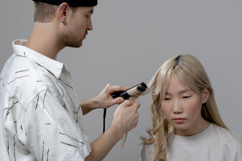 Man using a curling iron on a woman's hair