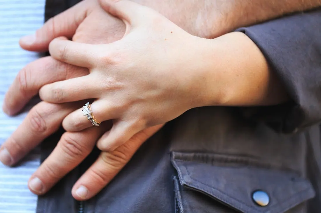Close up of a woman's hand with engagement ring holding a man's hand. 