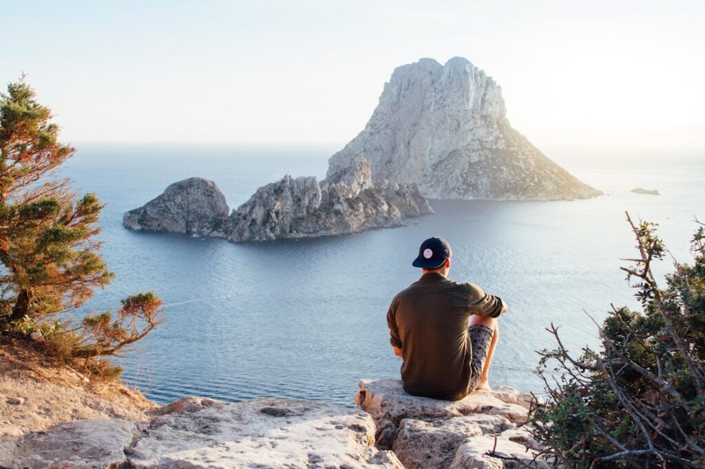 Man sitting on a cliff overlooking the sea reviewing things to keep in mind while on vacation