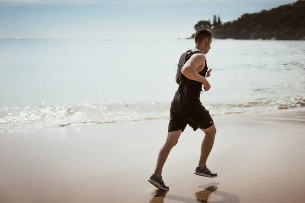 A man jogging on the beach taking advantage of the benefits of exercise in addiction treatment and recovery.