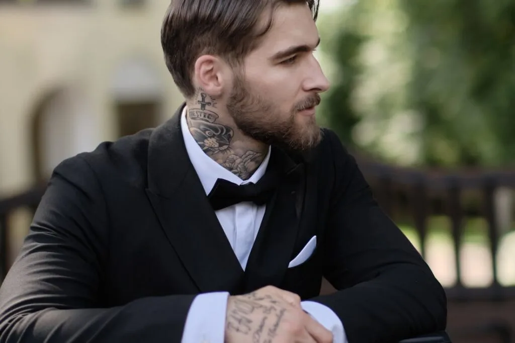 A man with tattoos wearing a tuxedo while sitting at a table