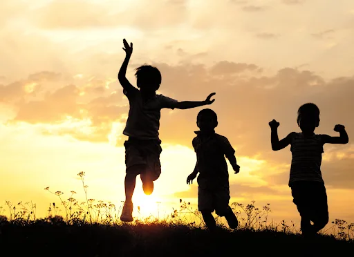 Silhouette of kids playing outside in the sun. Encouraging physical activity is one of the key parts of nurturing healthy habits in kids.