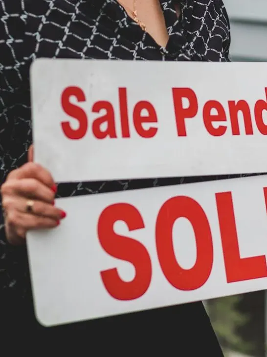 A woman holding a sale pending sold sign. Use these tips when selling your home as is.