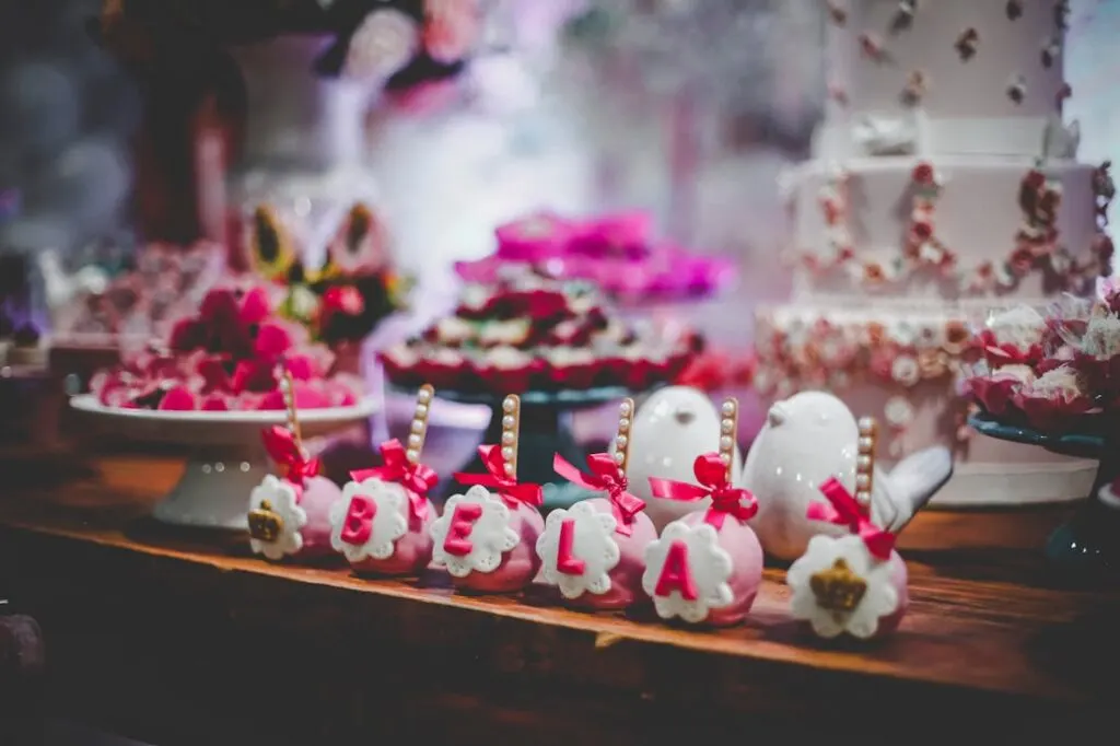 Pink and white cake balls on the front part of a table filled with cake and other foods for a kids birthday party.