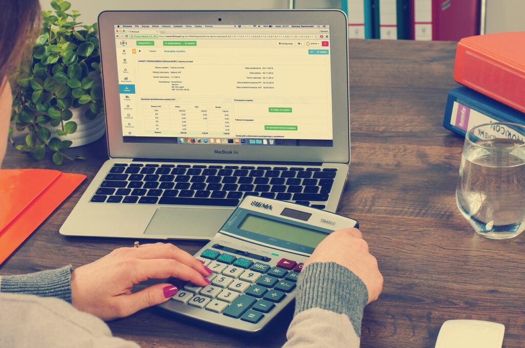 A woman using a calculator and laptop while working on tax obligations for freelancers.