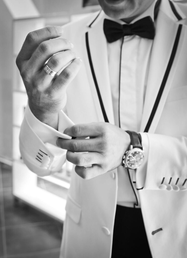 A black and white image of a man adjusting his cuffs after choosing the right tuxedo