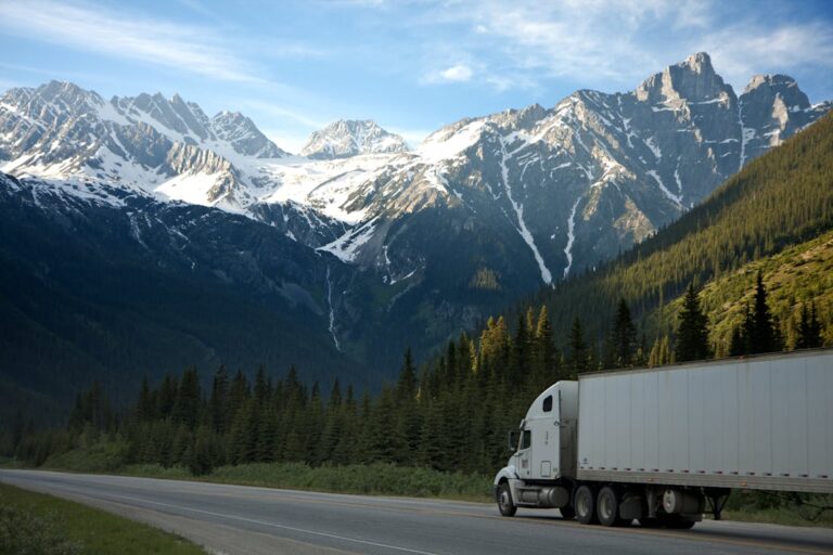A driver who choose a trucking career drives their truck down the highway with snow-capped mountains in the distance.
