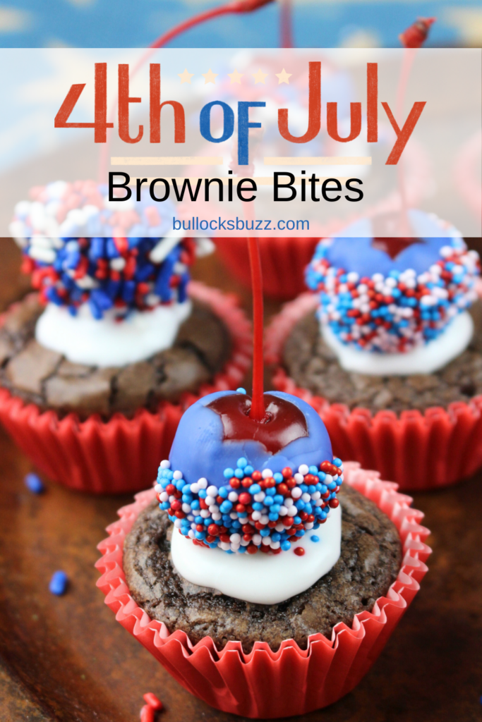 A close up image of a mini brownie bite topped with a cherry dipped in blue chocolate and red, white, and blue sprinkles. More patriotic brownie bites are behind it and slightly blurred.