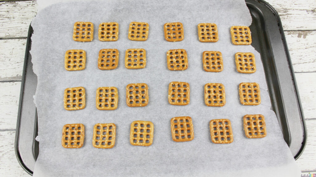 Pretzel squares laid out in rows on a parchment paper lined baking pan