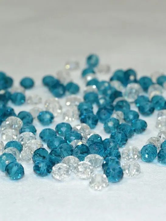 A pile of blue and clear acrylic beads on a white background. Learn the key differences between acrylic and crystal beads for your crafting projects