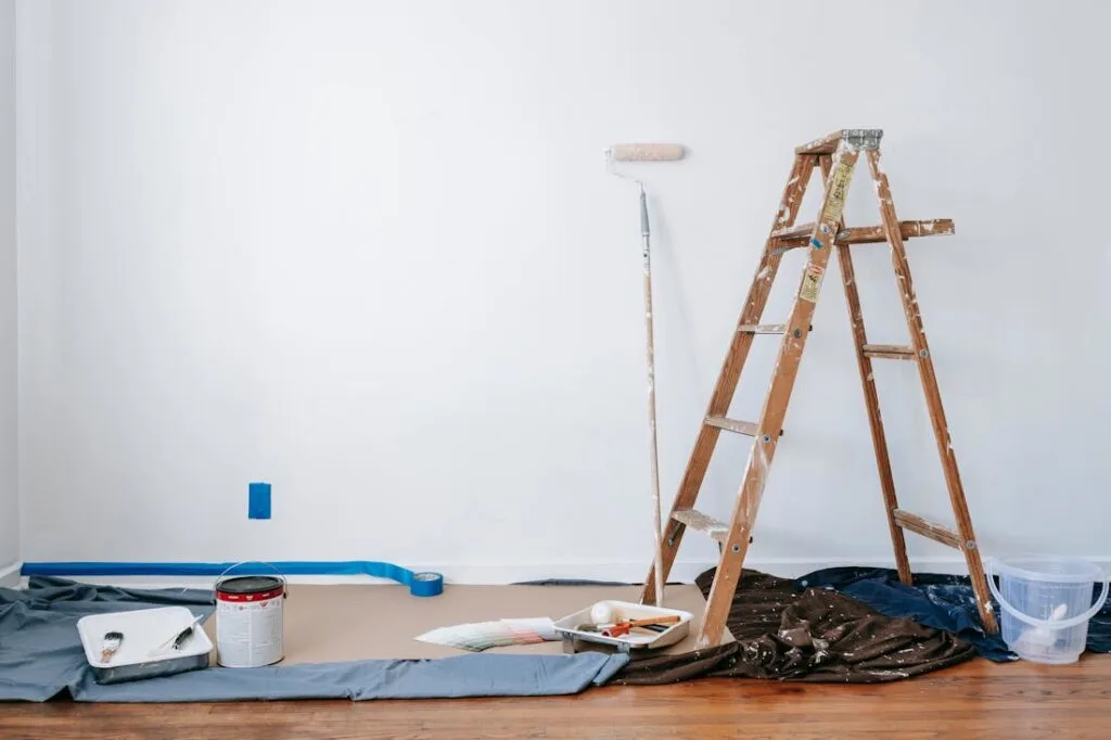A ladder, paint, paint rollers and tarp all tools needed for home renovation projects