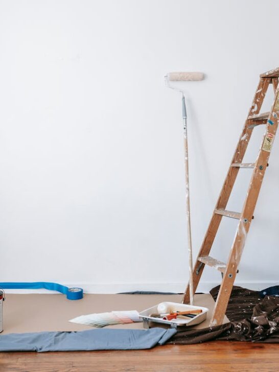 A ladder, paint, paint rollers and tarp all tools needed for home renovation projects