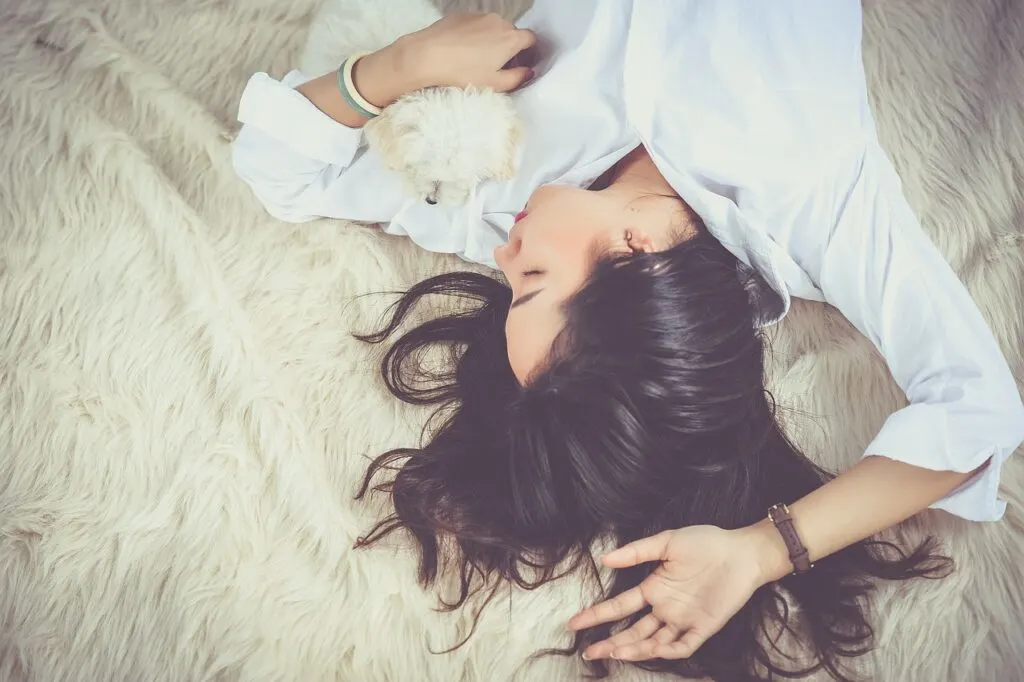 A woman in a white shirt laying on a blanket asleep. Comfort plays a big role in ways to improve your sleep pattern