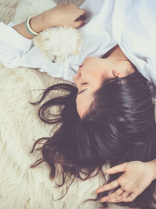 A woman in a white shirt laying on a blanket asleep. Comfort plays a big role in ways to improve your sleep patterns