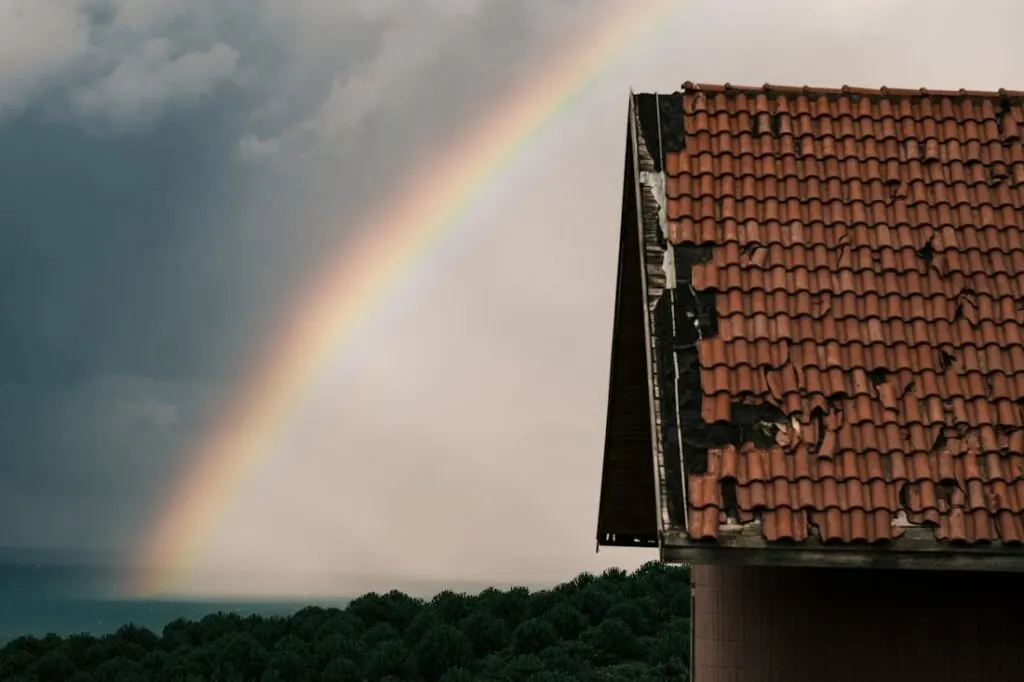 A damaged roof after a storm with a rainbow in the background. Understanding roof warranties is essential as a homeowner to protect your investment.