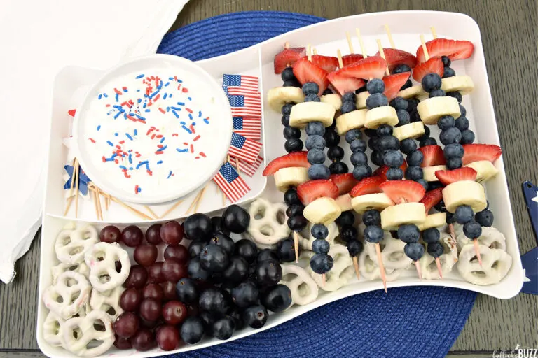 Fruit kabobs and a bowl of patriotic fruit dip on a flag shaped tray
