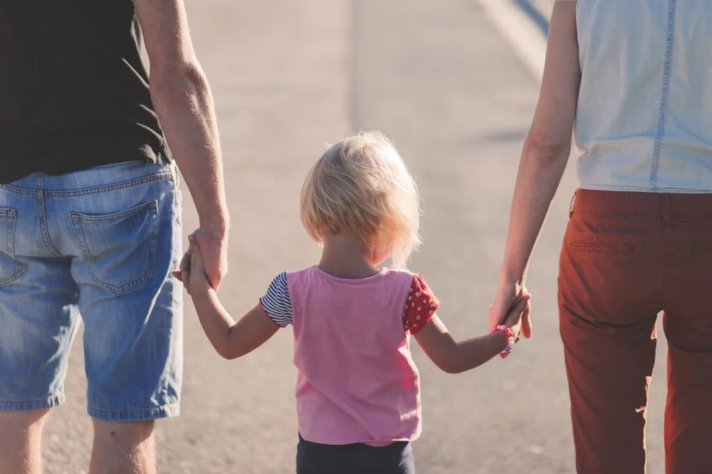 A little girl walking in between her parents holding their hands is a great example of parent providing security and stable family homes for kids.