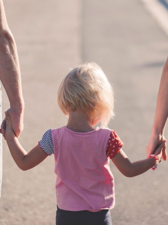 A little girl walking in between her parents holding their hands is a great example of parent providing security and stable family homes for kids.