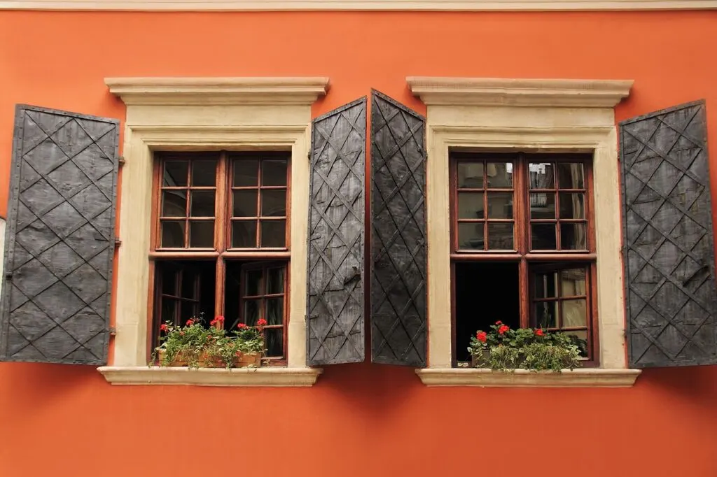 A set of wood windows with open shutters on an orange home. Use these tips to repair and maintain wood windows to keep yours in great shape!