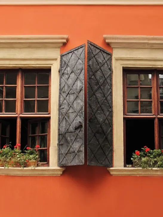 A set of wood windows with open shutters on an orange home. Use these tips to repair and maintain wood windows to keep yours in great shape!