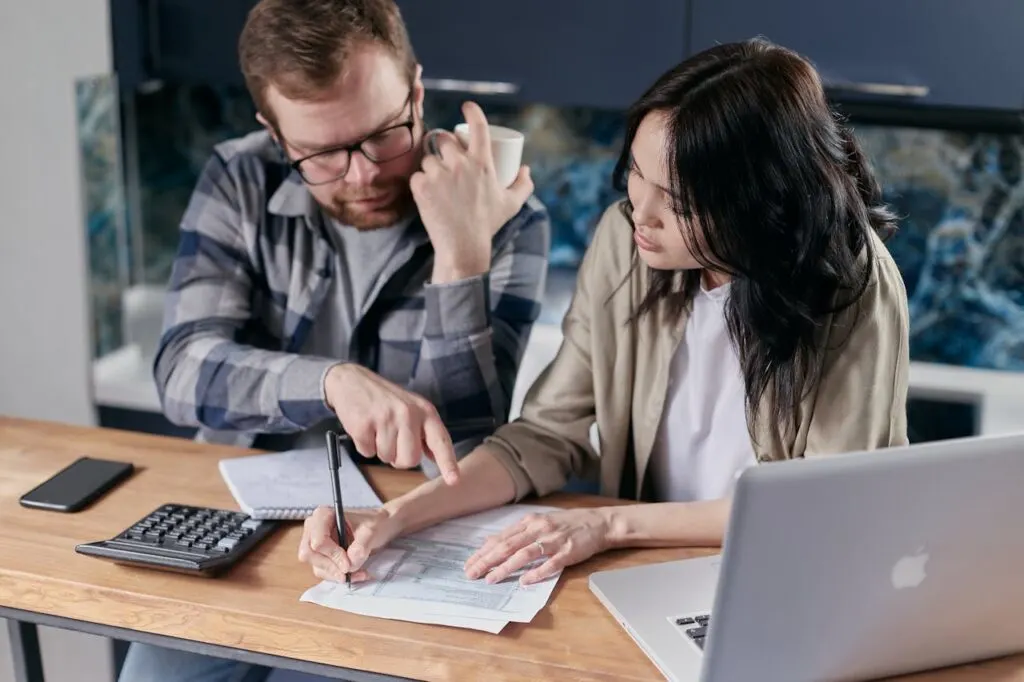a couple sitting at a table managing finances using paper and laptop