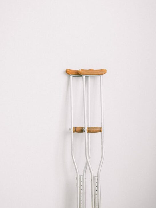 A pair of crutches against a white wall. Crutches are often part of Key Steps to Improving Health Post-Injury