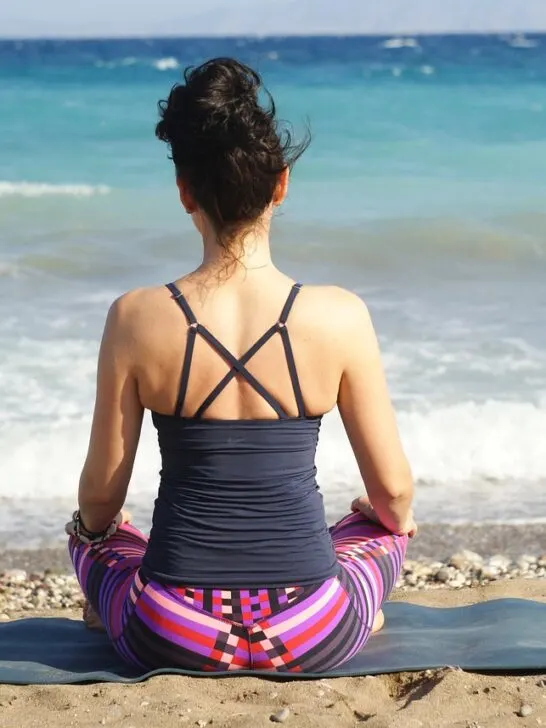 A woman sitting on the beach facing the water and meditating as a way of practicing digital mindfulness