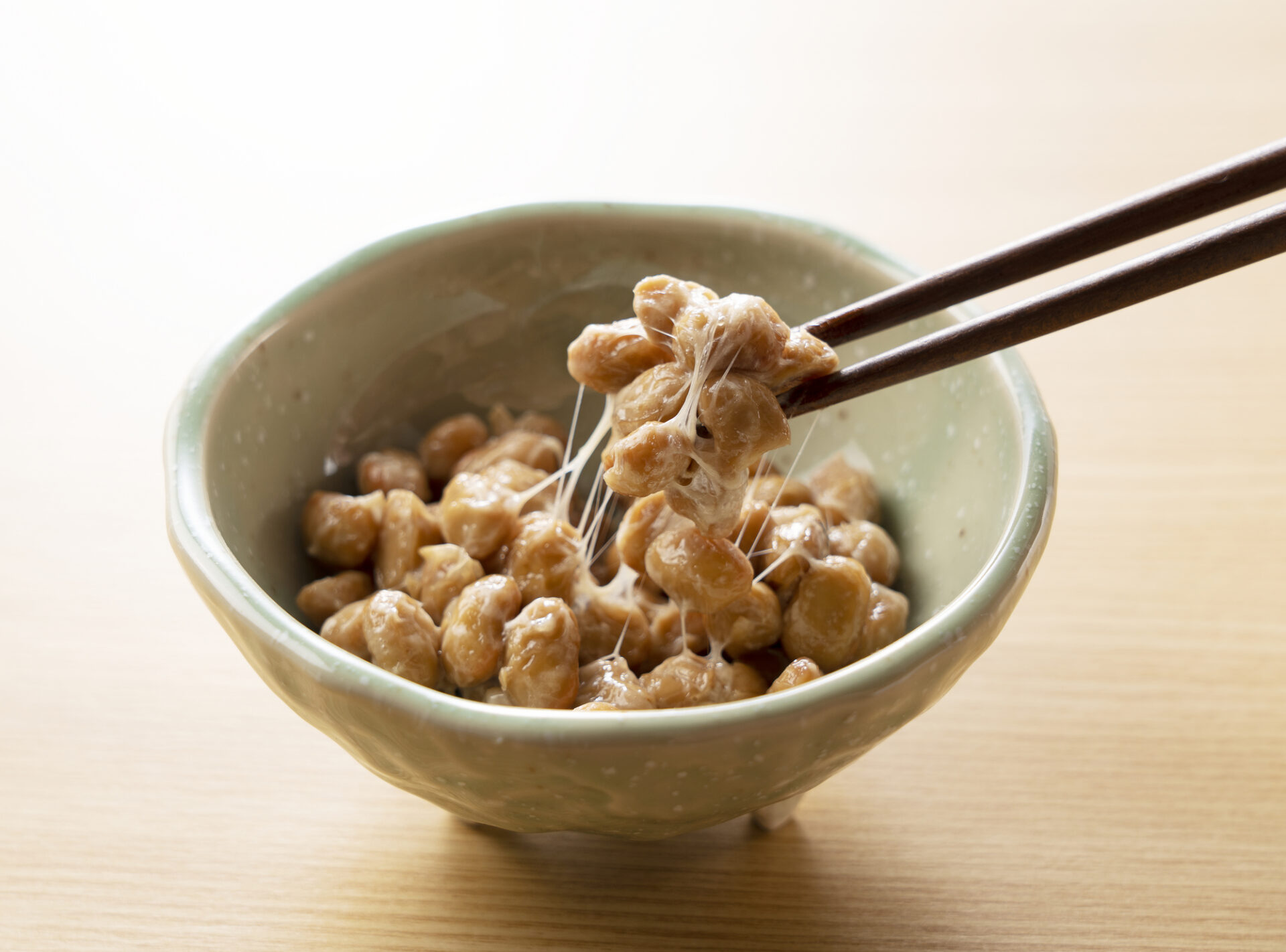 Natto in a plate set against a wooden background is lifted with chopsticks