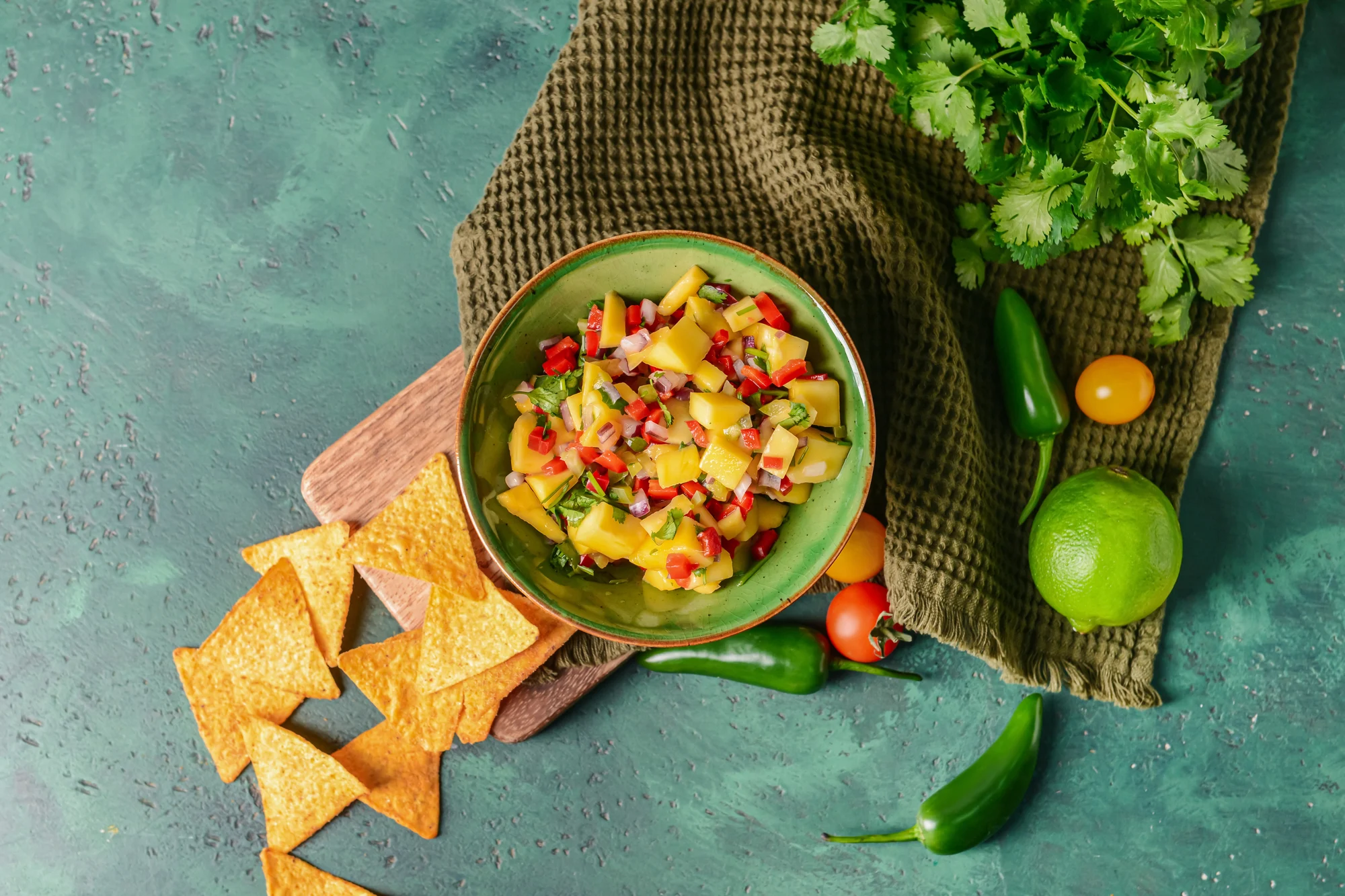 Bowl with fresh mango salsa and nachos on color background