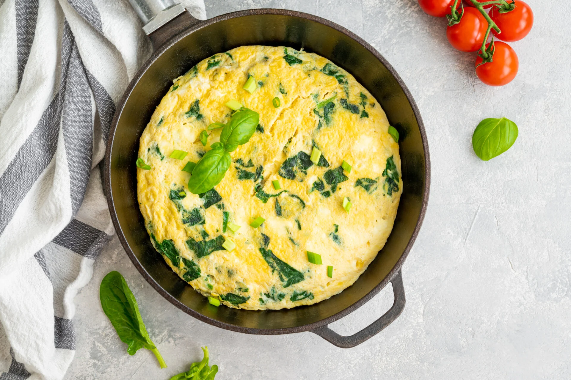Omelette with spinach, green onions and feta cheese in a cast-iron frying pan on a gray concrete background. Healthy breakfast. Top view, copy space