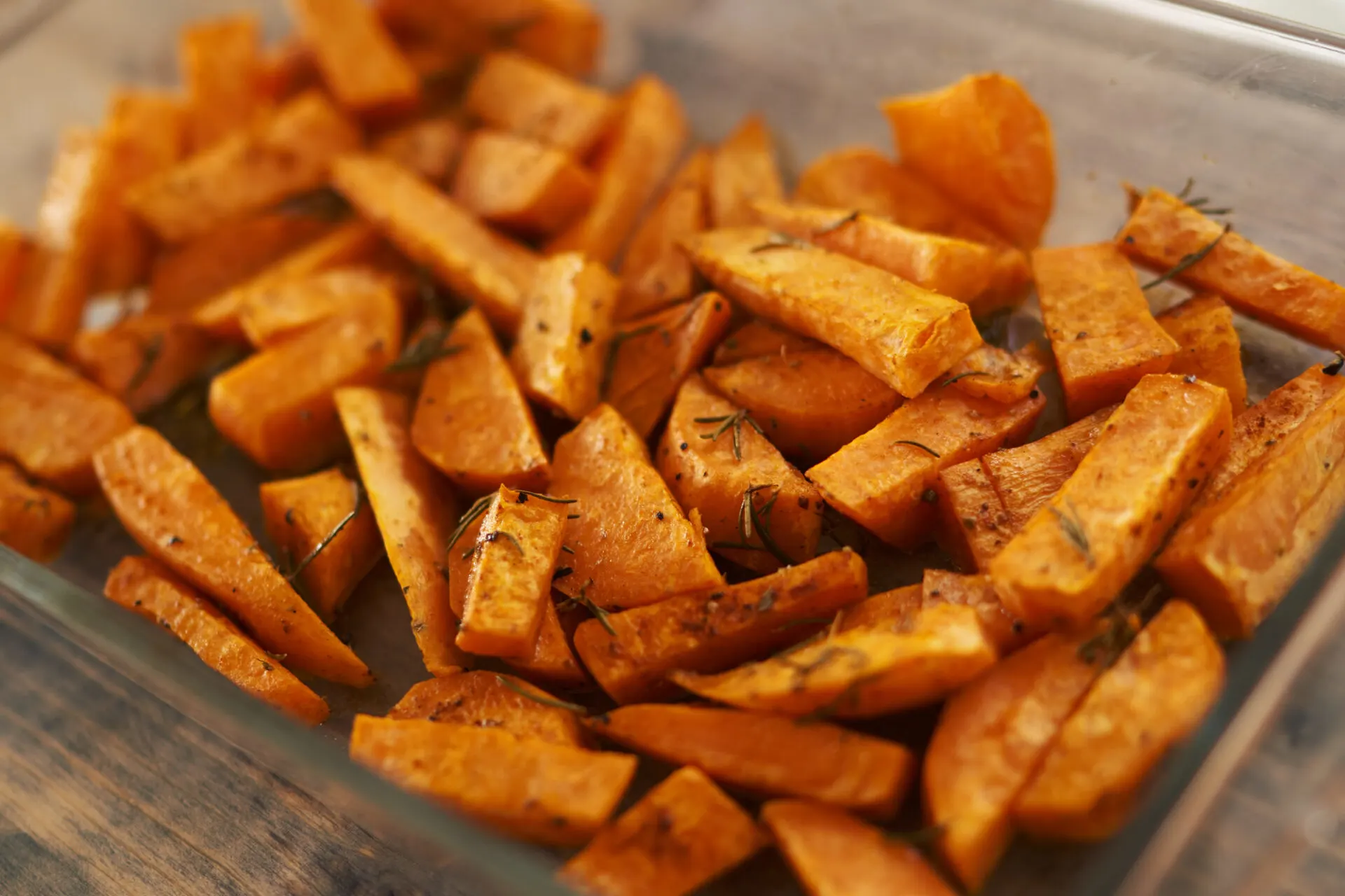 Sweet potatoes baked with rosemary in a glass bowl stand on the table