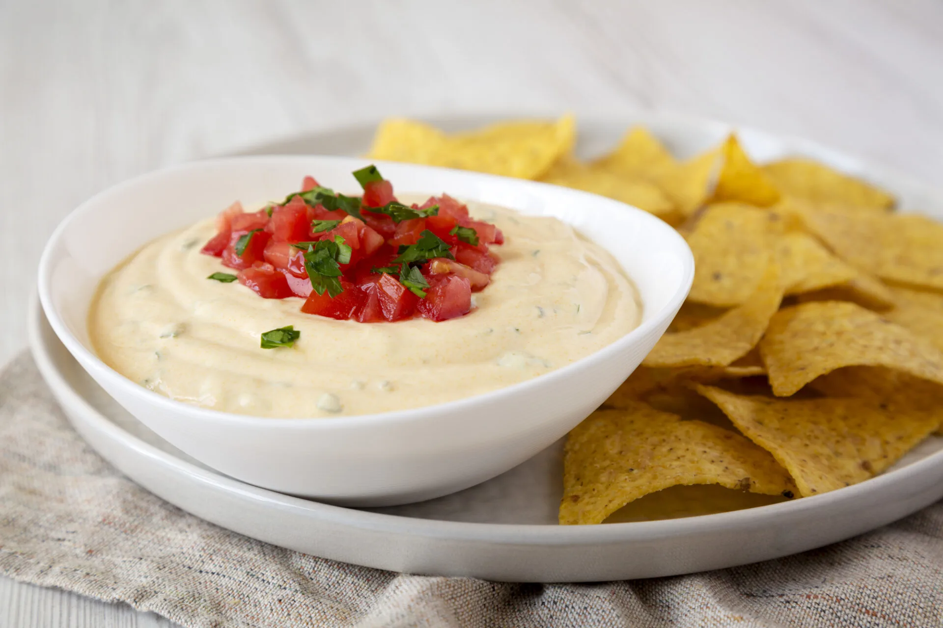 Homemade cheesy dip in a bowl, yellow tortilla chips, side view. Close-up.
