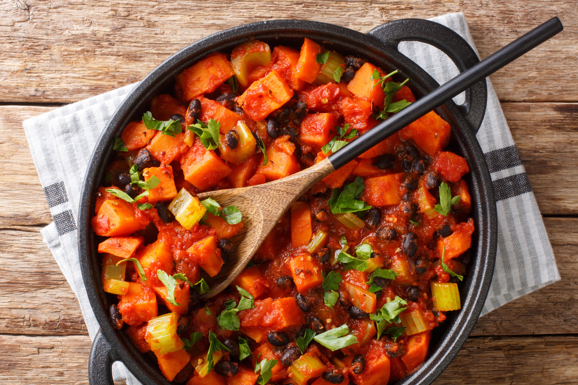 Chili sweet potatoes and black beans with tomatoes, celery close-up in a pan on the table. Horizontal top view from above