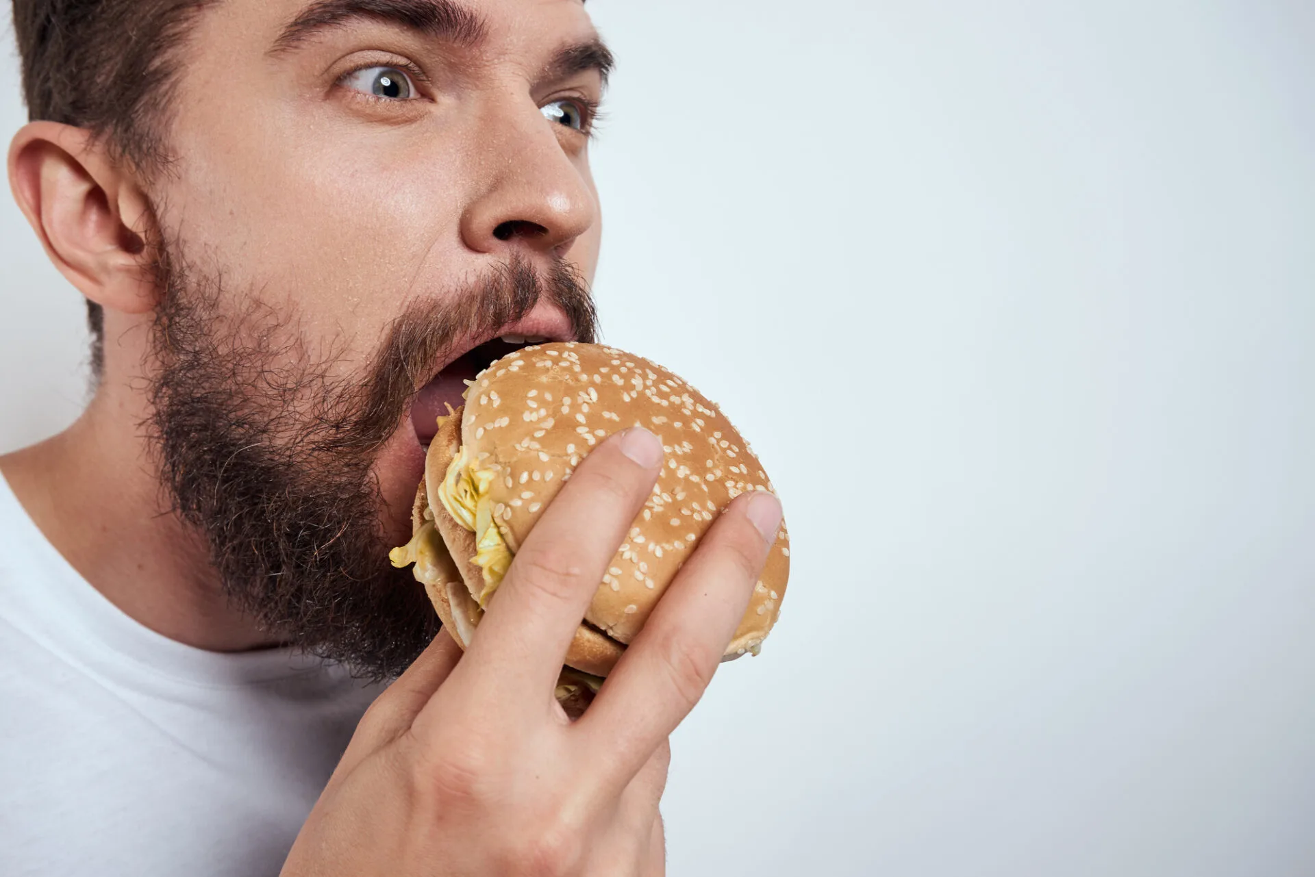 A man eating a hamburger on a light background in a white T-shirt cropped view close-up hunger fast food. High quality photo
