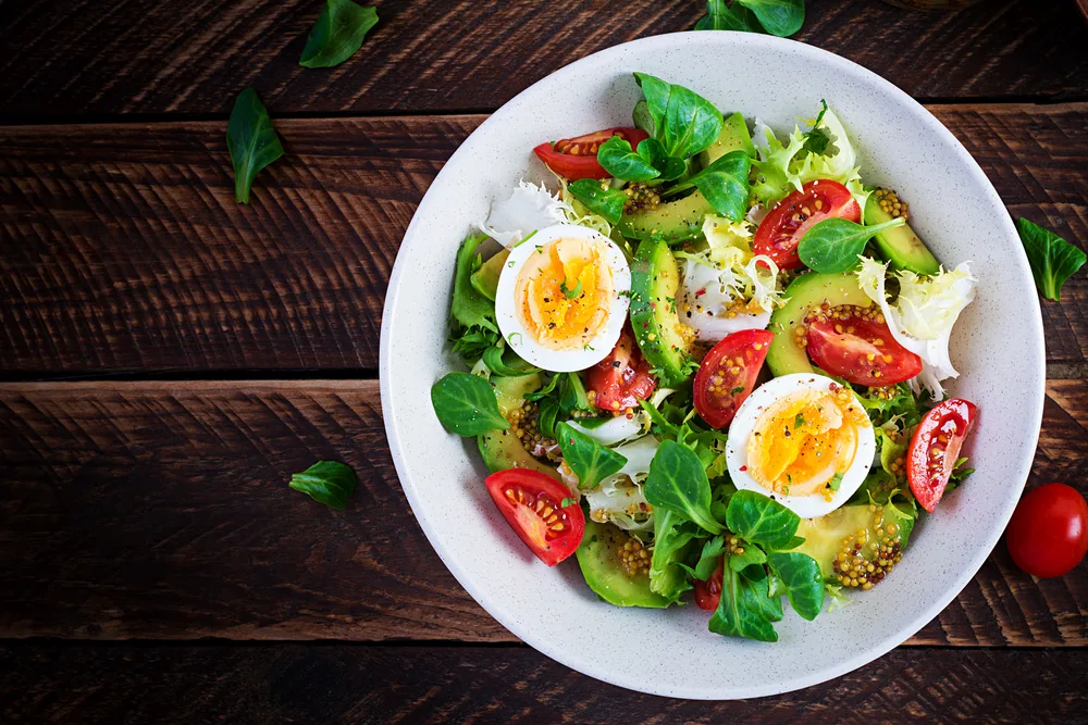 Fresh avocado salad with tomato, avocado, boiled eggs and fresh lettuce. Ketogenic diet breakfast. Keto, paleo salad. Top view, overhead, above