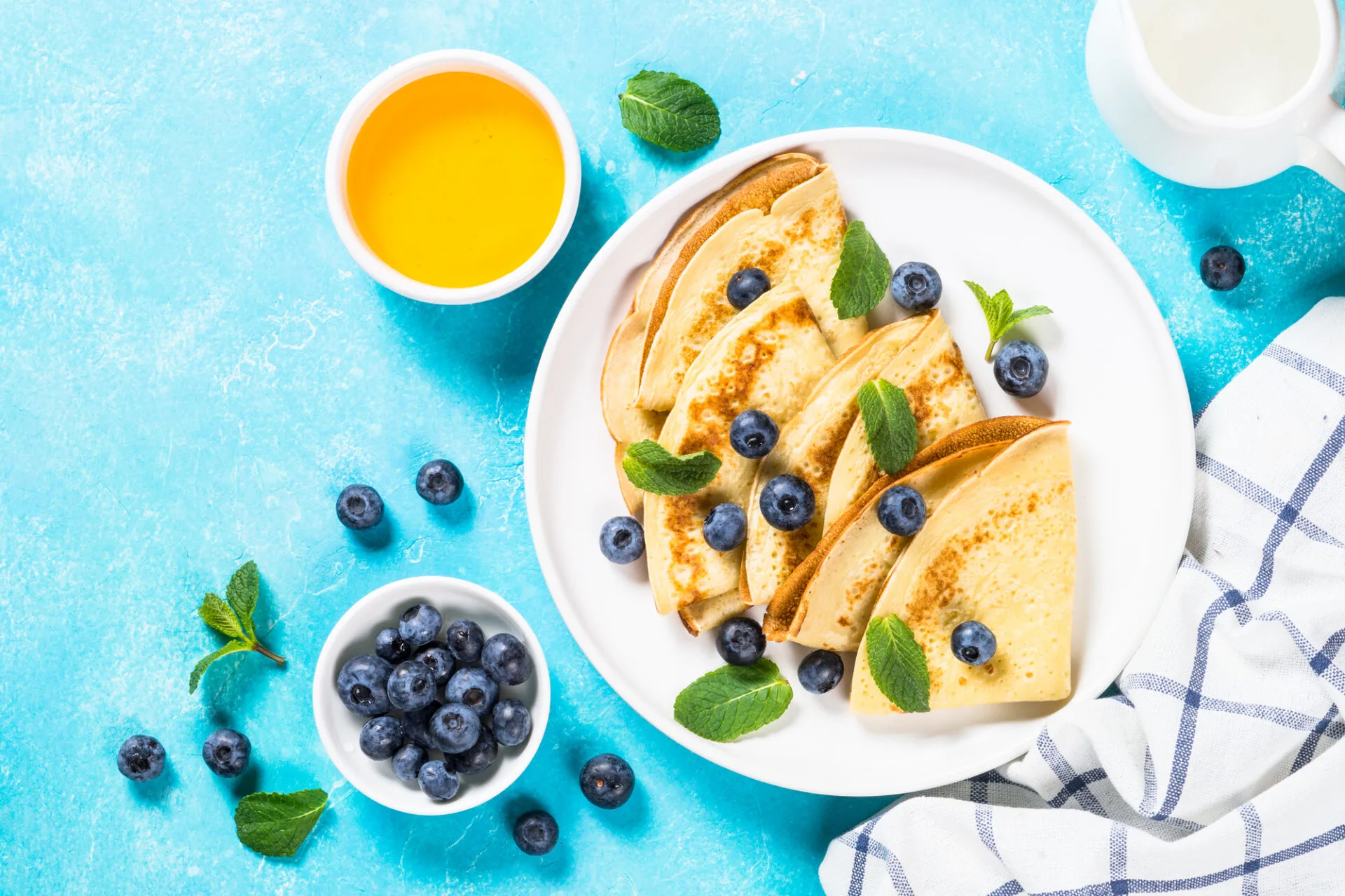 Crepes with blueberries and honey in white plate at blue table. Top view with copy space.