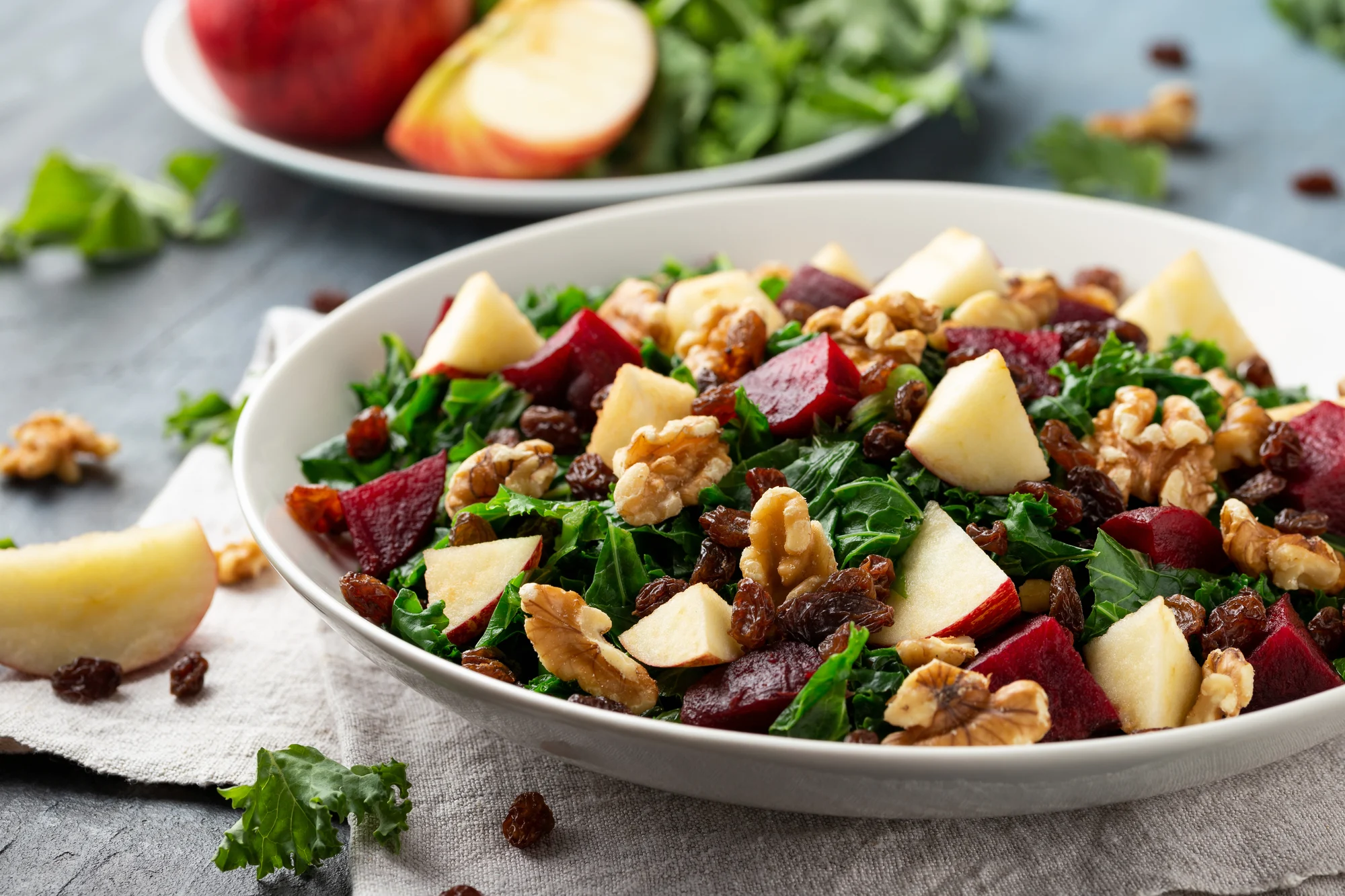 Kale salad with apple, beetroot, walnut and raisins in white plate. Healthy food.