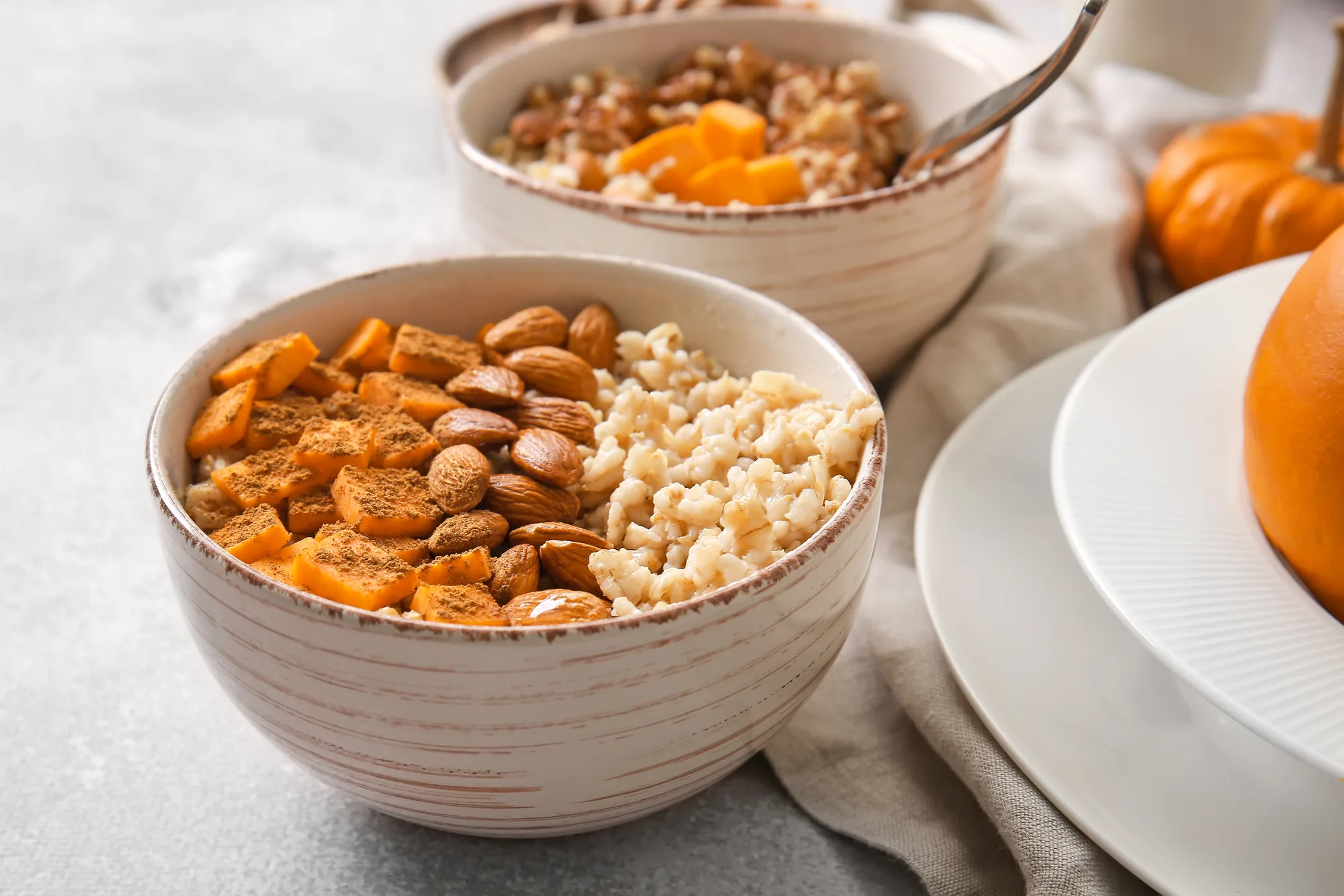 Bowls of tasty oatmeal with pumpkin and almond on light background