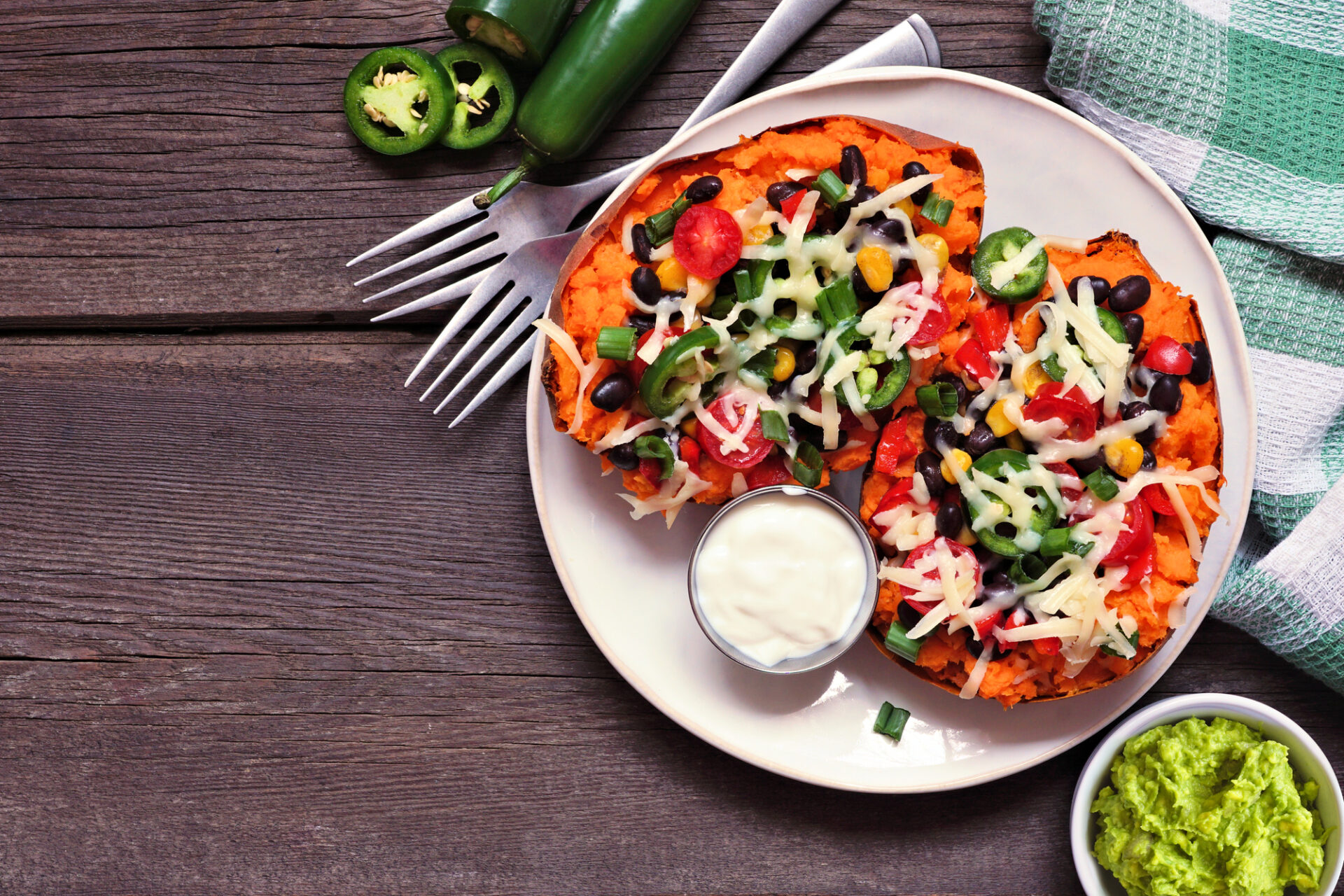 Baked sweet potato tacos stuffed with black beans, vegetables and cheese. Top view table scene on a dark wood background.
