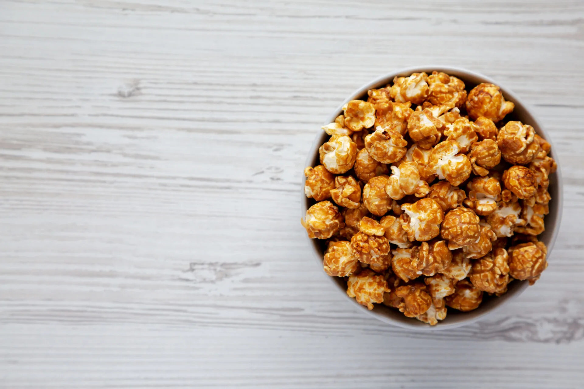 Homemade Caramel Popcorn in a gray Bowl on a white wooden surface, top view. Flat lay, overhead, from above. Space for text.