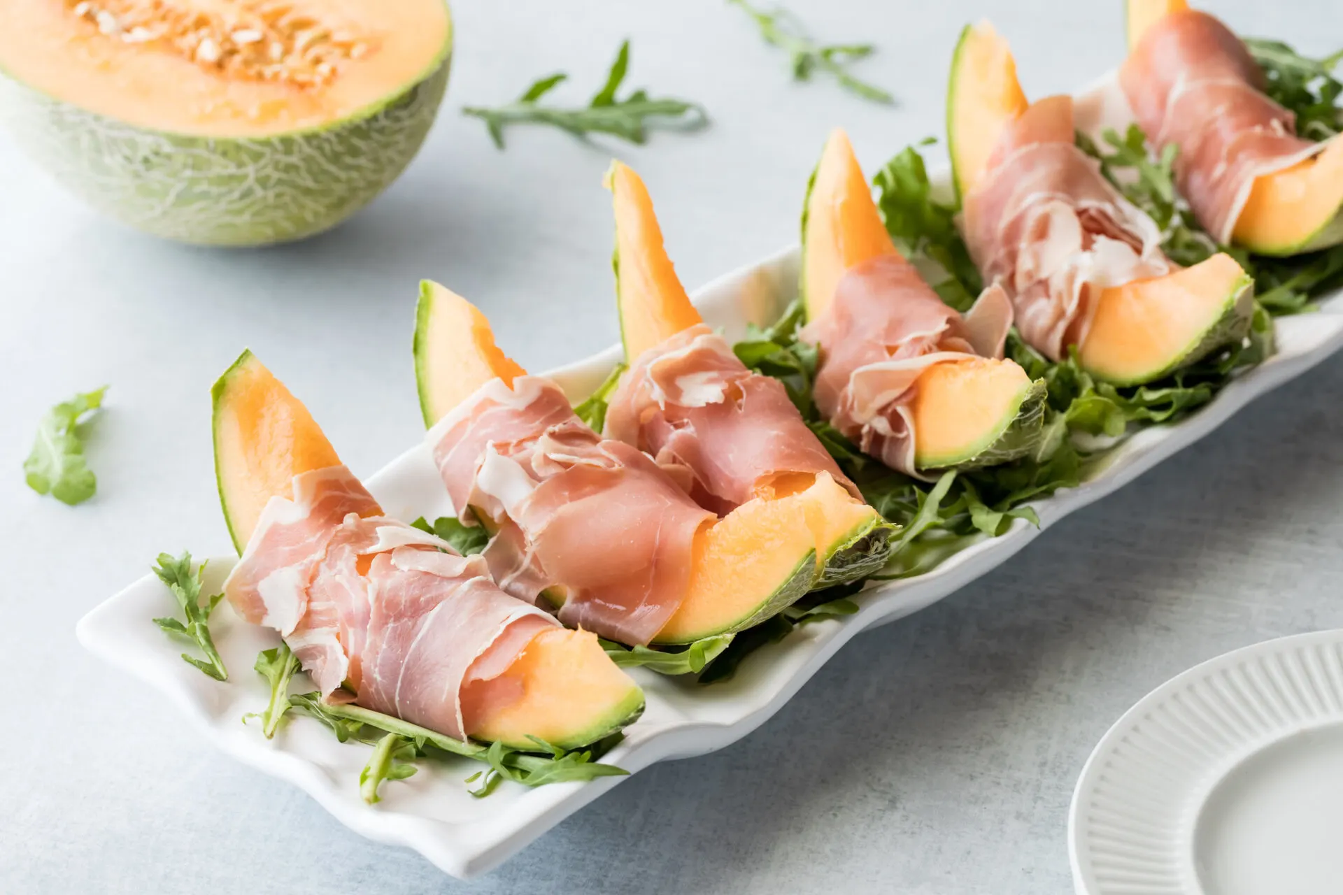 Above view of prosciutto wrapped cantaloupe slices on a platter of arugula.
