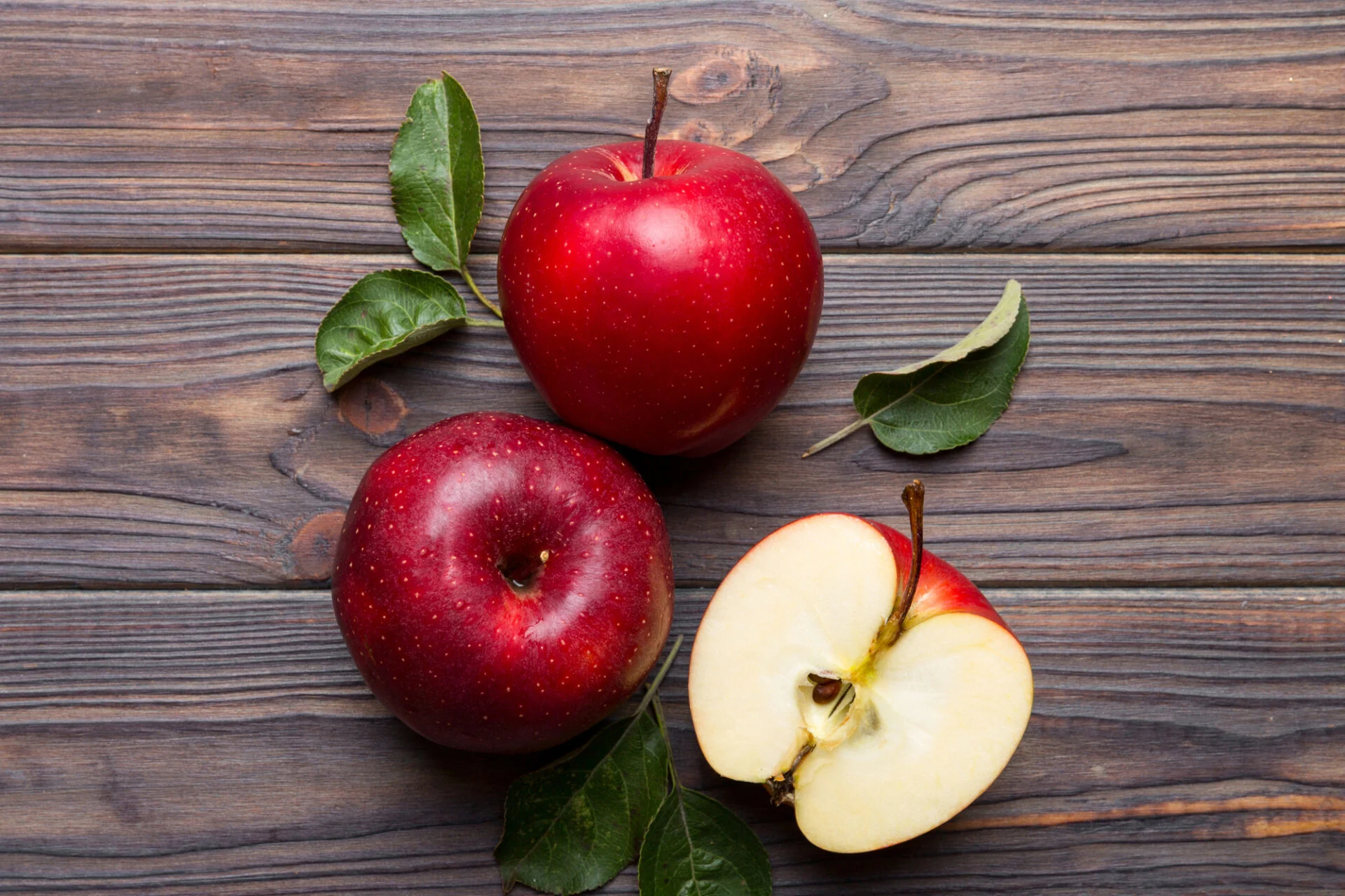 Fresh red apples with green leaves on wooden table. On wooden background. Top view free space for text.