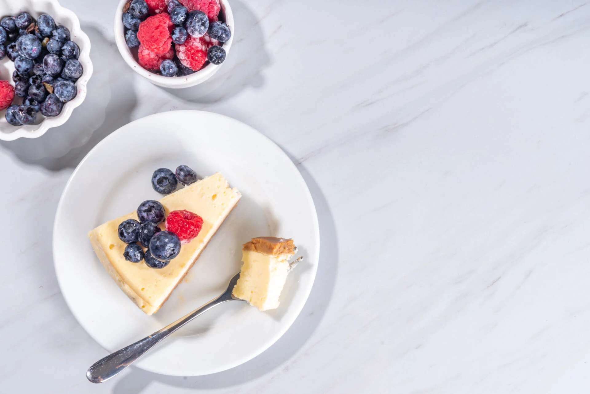 Cheesecake portion slice on plate, with raspberry on blueberry on white marble background