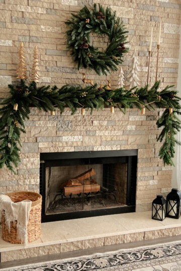 The King Noble Fir Collection shown here in front of a brick fireplace with the garland on the mantel, the wreath hanging above the mantle, and two small trees on each side of the hearth.