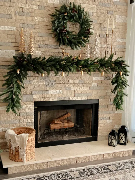 The King Noble Fir Collection shown here in front of a brick fireplace with the garland on the mantel, the wreath hanging above the mantle, and two small trees on each side of the hearth.