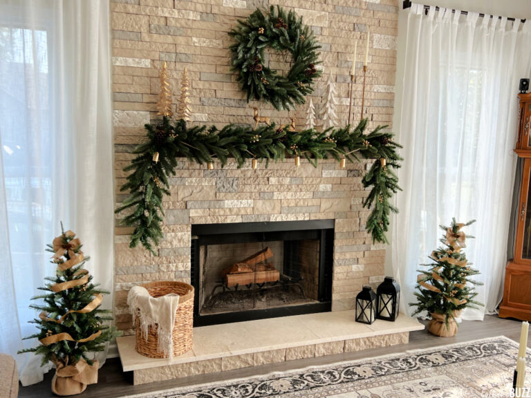 The King Noble Fir Collection shown here in front of a brick fireplace with the garland on the mantel, the wreath hanging above the mantle, and two small trees on each side of the hearth.